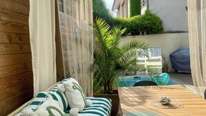 A wooden deck with a striped sofa, a table, and a covered area with curtains. - Nice town house, 4 mn from Bordeaux Rive droite Private swimming pool (Cenon)