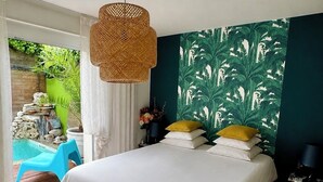 A bedroom with a bed, a hanging light fixture, a nightstand, and a view of an outdoor pool area. - Nice town house, 4 mn from Bordeaux Rive droite Private swimming pool (Cenon)