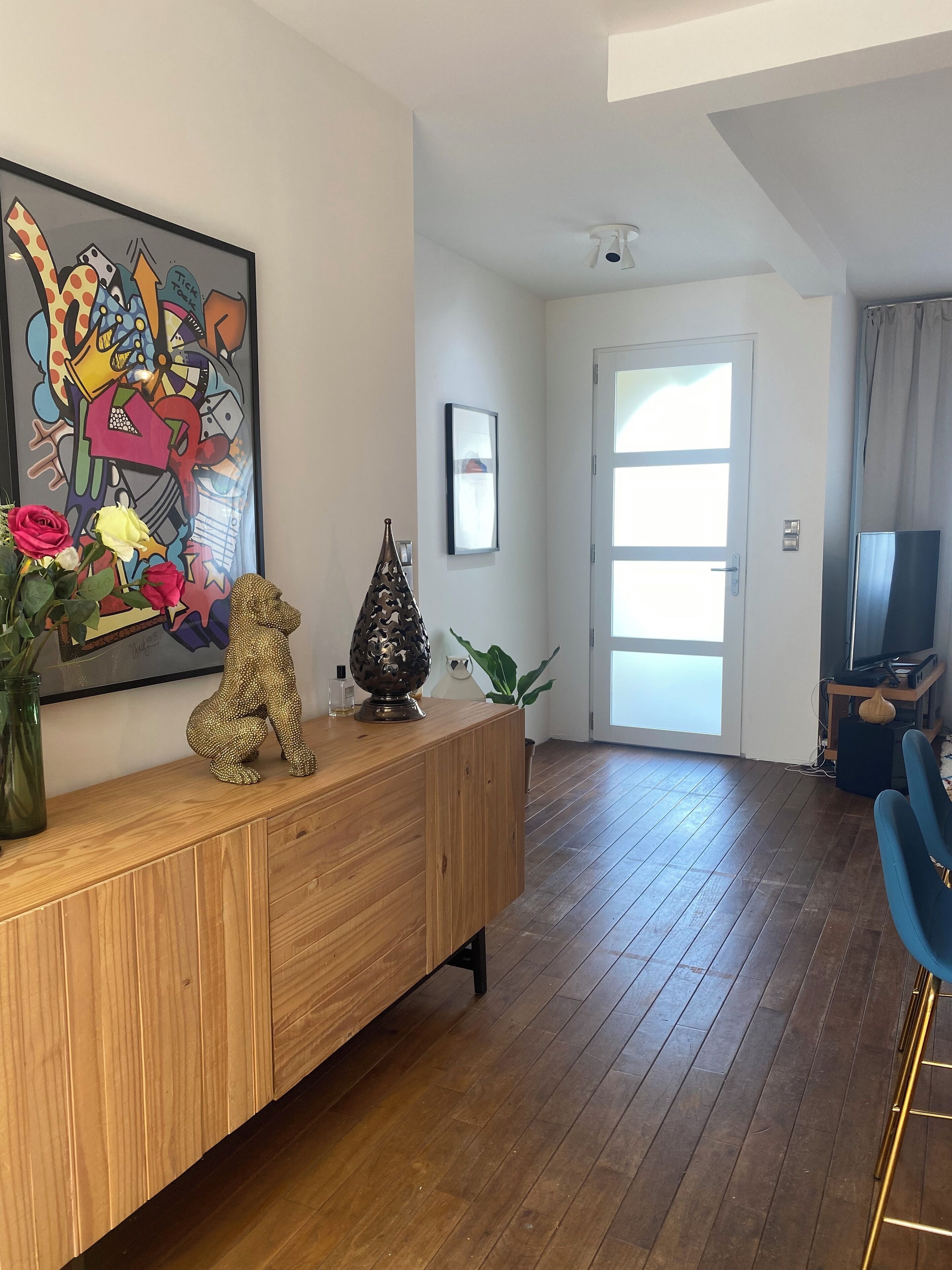 Una sala de estar moderna con una consola de madera, un cuadro abstracto y colorido, una escultura decorativa de un animal y un ventanal grande.