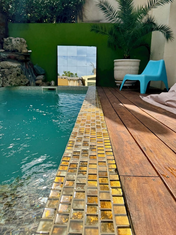 A swimming pool with a tiled edge, a wooden deck, a blue chair, and a potted plant.