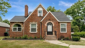 A two-story brick house with a front porch, a chimney, and a small front yard. - 3BR Near Cleveland & CVNP | Sunroom + Ping-Pong (Independence)