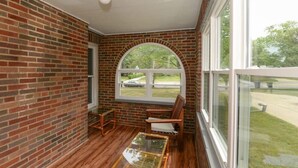 A room with brick walls, a wooden floor, a glass table, and a window with a view of a car and greenery outside. - 3BR Near Cleveland & CVNP | Sunroom + Ping-Pong (Independence)