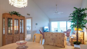 A spacious living room with a round table, floral sofa, and a wooden cabinet with glass doors. - Perico Bay Club · 30-Night Min · Intracoastal (Bradenton)