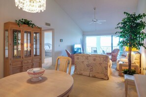 A spacious living room with a round table, floral sofa, and a wooden cabinet with glass doors.