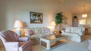 A living room with a sofa, armchair, and coffee table, a painting on the wall, and a chandelier. - Perico Bay Club · 30-Night Min · Intracoastal (Bradenton)