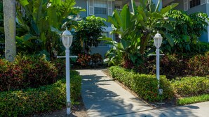 A pathway leading to a building with a covered entrance, surrounded by lush greenery and two white street lamps. - Perico Bay Club · 30-Night Min · Intracoastal (Bradenton)