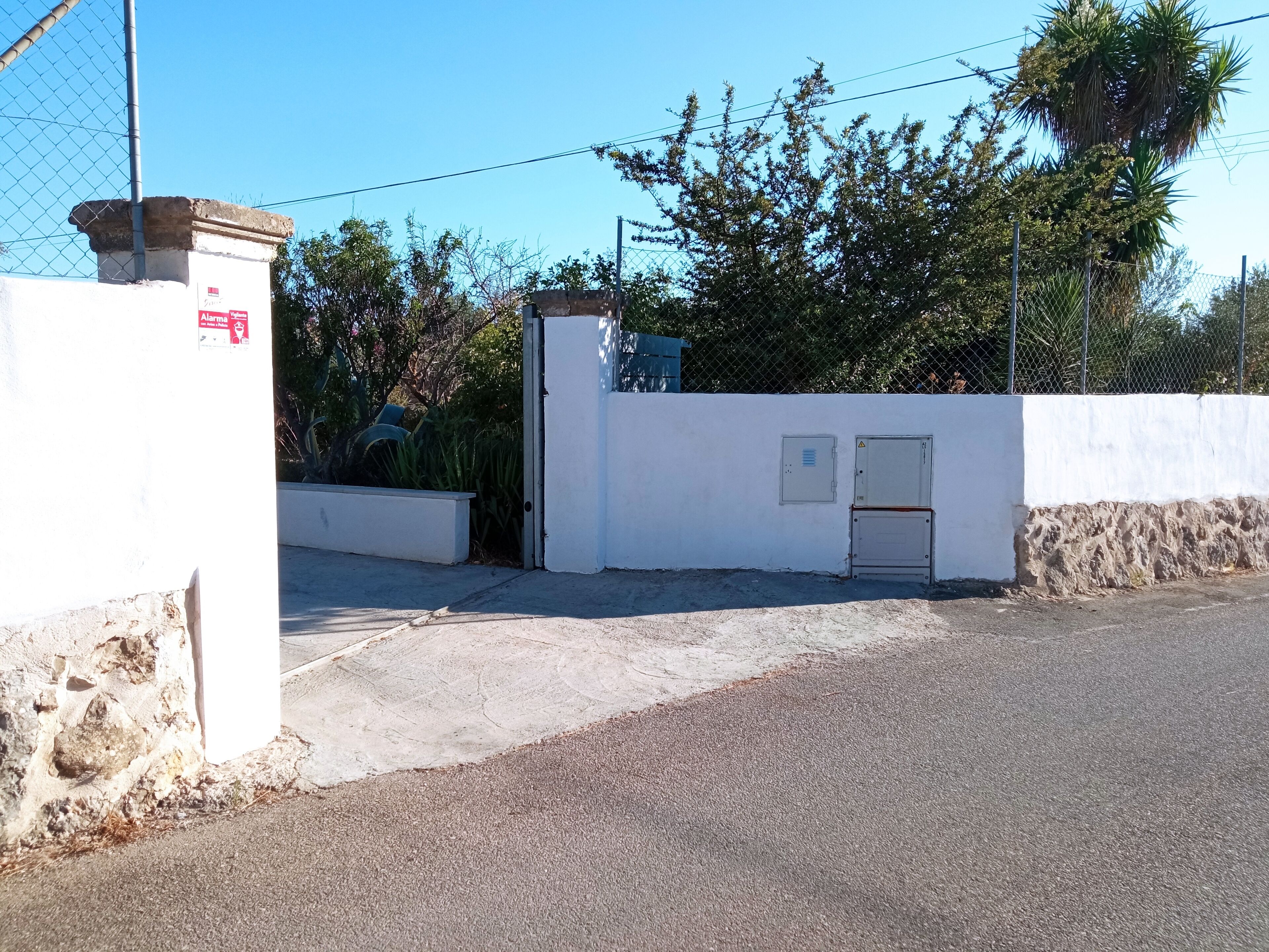 A gated entrance with a white wall, a metal gate, and a small utility box.