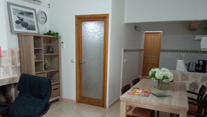 A dining area with a wooden table, chairs, and a vase of flowers. There is a wooden cabinet and a bookshelf with various items. - Can Barcelo (Inca)