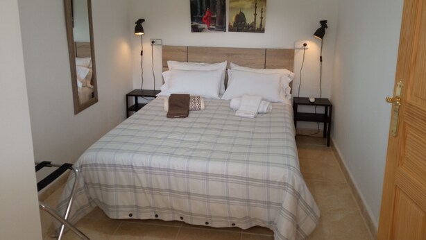 A neatly made bed with a plaid bedspread, two bedside tables with lamps, a mirror on the wall, and a door to the right. - Can Barcelo (Inca)
