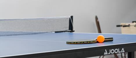 A table tennis table with a net, a paddle, and a ball.