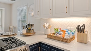 A modern kitchen with white cabinets, a gas stove, and a countertop with a basket of snacks and a knife block. - Airy 5br home w/pool, outdoor living, game room (Mobile)