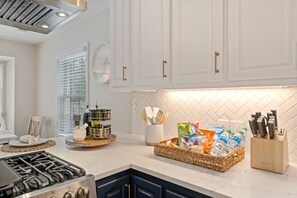 A modern kitchen with white cabinets, a gas stove, and a countertop with a basket of snacks and a knife block.