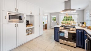 A modern kitchen with white cabinetry, a stainless steel microwave, a gas stove, and a built-in oven. - Airy 5br home w/pool, outdoor living, game room (Mobile)