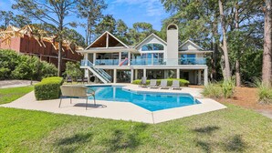 Ein zweistöckiges Haus mit Swimmingpool, umgeben von Bäumen und einem gepflegten Rasen.