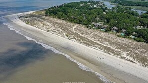 Eine Luftaufnahme einer Küstenregion mit einem Sandstrand, einer bewaldeten Halbinsel und einem Gewässer.