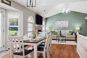 A dining area with a table set for four, a fireplace, and a living room with a sofa and a large floral painting.