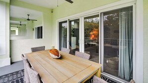 Ein Essbereich mit Holztisch und Korbstühlen, einem Deckenventilator und einer Glasschiebetür, die zu einer Außenpatio führt.