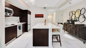 A modern kitchen with a central island, dark cabinetry, and white countertops. - Villa Vista by VIAC - 2 Story w/ 3Bdrms & Golf View (Doral)