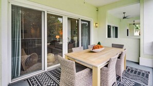 Ein Essbereich mit Holztisch, Korbstühlen, großen Schiebeglasfenstern, Deckenventilatoren und einem gemusterten Teppich.