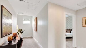 A hallway with a desk, chairs, and artwork on the walls. There is a door leading to a bedroom with a bed and pillows. - Villa Vista by VIAC - 2 Story w/ 3Bdrms & Golf View (Doral)