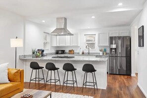 A modern kitchen with white cabinetry, a stainless steel range hood, and a central island with bar stools.