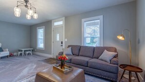 Ein Wohnzimmer mit grauem Sofa, einem Couchtisch mit einer Vase, einer Stehlampe und einem Fenster mit Jalousien.