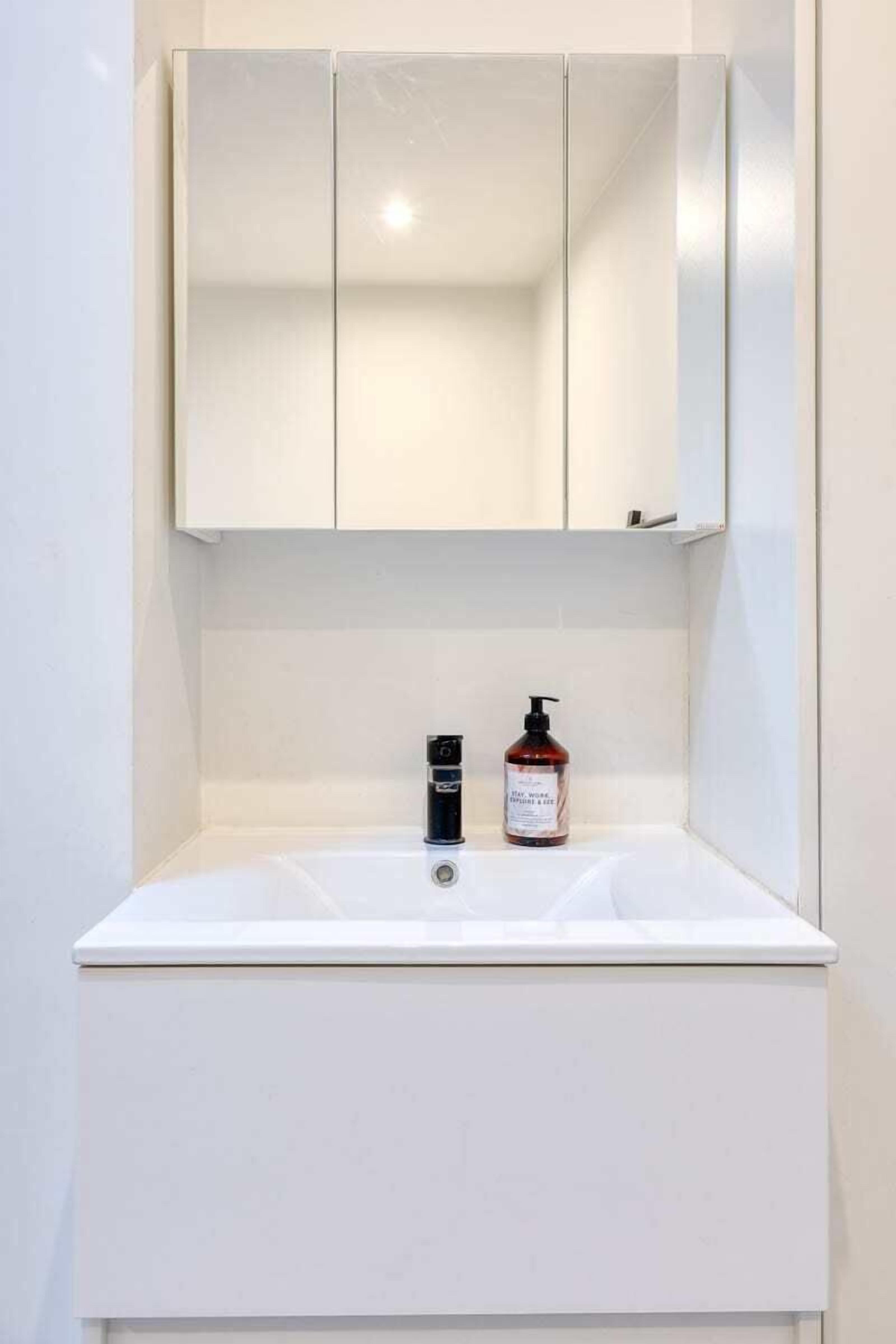 A white bathroom with a mirror above a sink and two bottles on the counter.