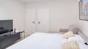 Un dormitorio moderno con una cama grande, un televisor sobre un mueble y dos puertas blancas.