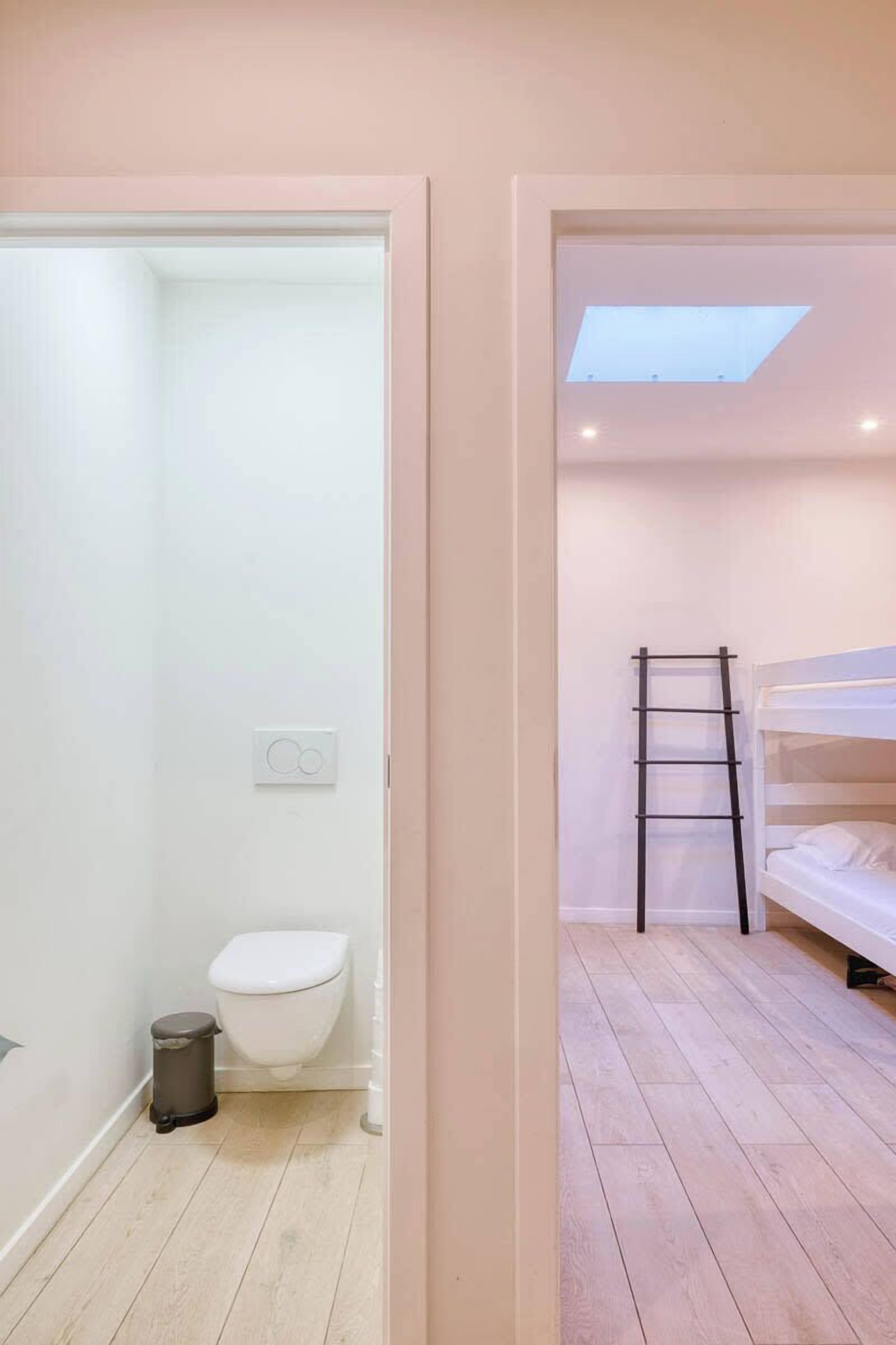 Een kleine, moderne kamer met een stapelbed, dakraam en een apart toilet.