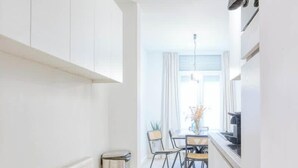 Una cocina moderna con armarios blancos, un comedor con mesa y sillas, y un ventanal con cortinas.