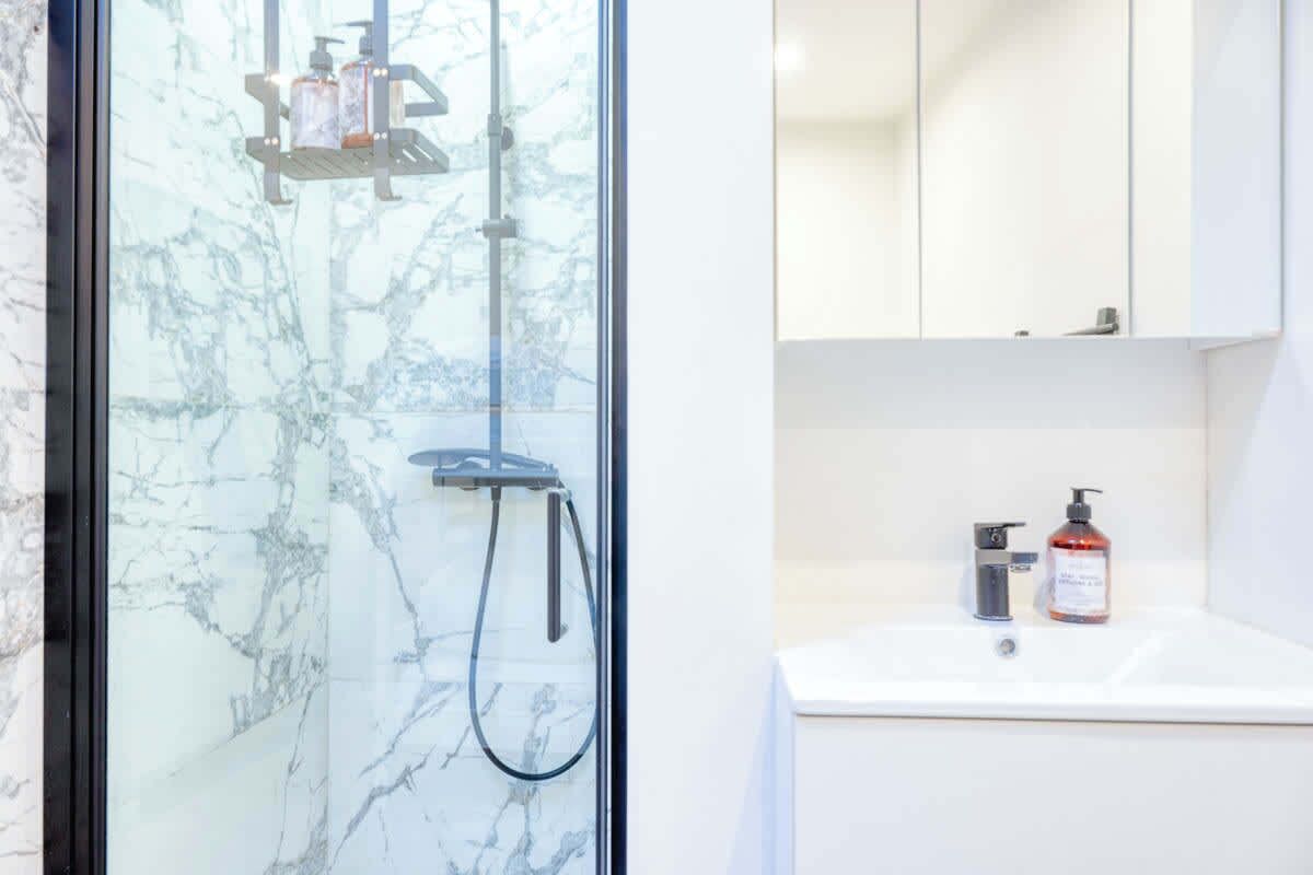 Un bagno moderno con doccia vetro, lavandino bianco e specchio soprastante.