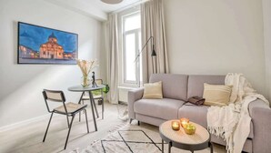 Ein modernes Wohnzimmer mit einer Couch, einem Esstisch mit Stühlen, einer Lampe und einem Gemälde eines Gebäudes.