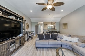 A spacious living room with a large sectional sofa, a flat-screen TV, a wooden entertainment unit, and a ceiling fan. - Mariner’s Club, Key Largo Home!!! 4bedroom 4bathroom Tropical Oasis (Key Largo)