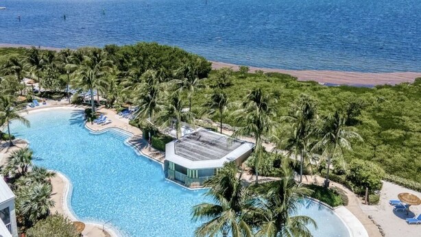 Een resort met een zwembad, palmbomen en uitzicht op het strand.