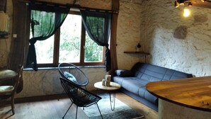 Ein rustikaler Raum mit Steinwand, Holzbalkendecke, einem schwarzen Metallstuhl, einem blauen Sofa und einem kleinen runden Tisch.