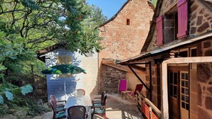 Ein rustikaler Außenbereich mit Tisch und Stühlen, einem Grill und einem Steinhaus mit einem Strohdach.