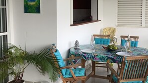 A dining area with a table set for four, surrounded by wooden chairs with blue cushions. A potted plant is visible to the left.