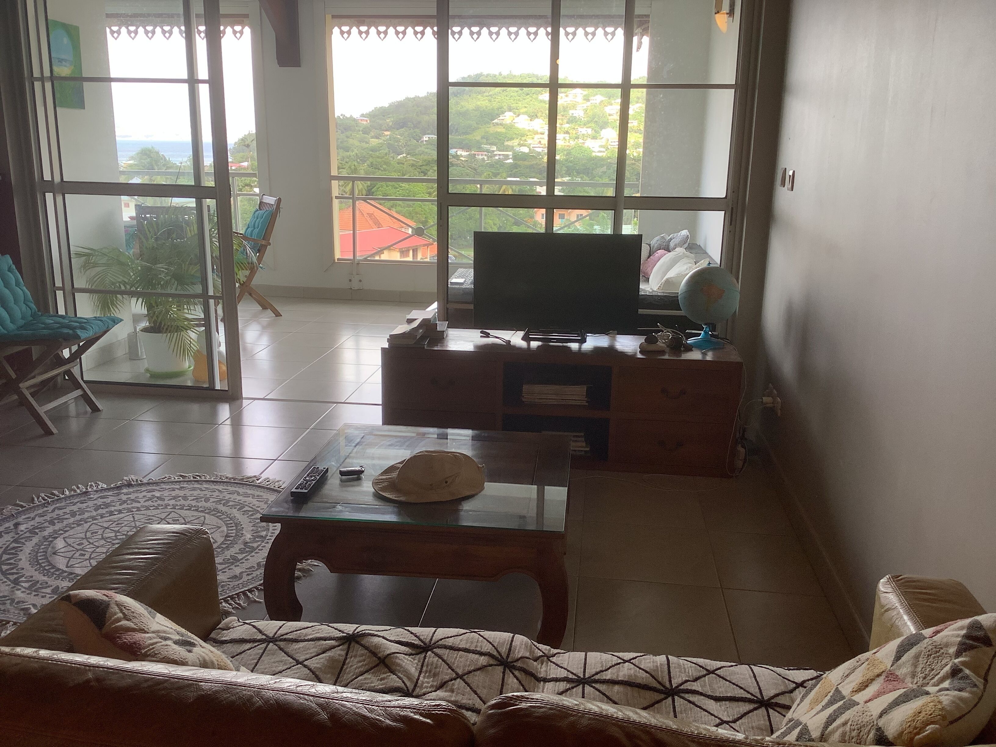 A living room with a sofa, a coffee table, a TV, and a view of a hillside.