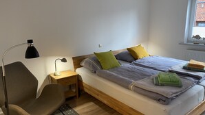 A bedroom with a bed, a desk with a lamp, a chair, and a window with a view of a building. - Family vacation near the North Sea near Büsum. Great day trips with children on the agenda. (Heide)