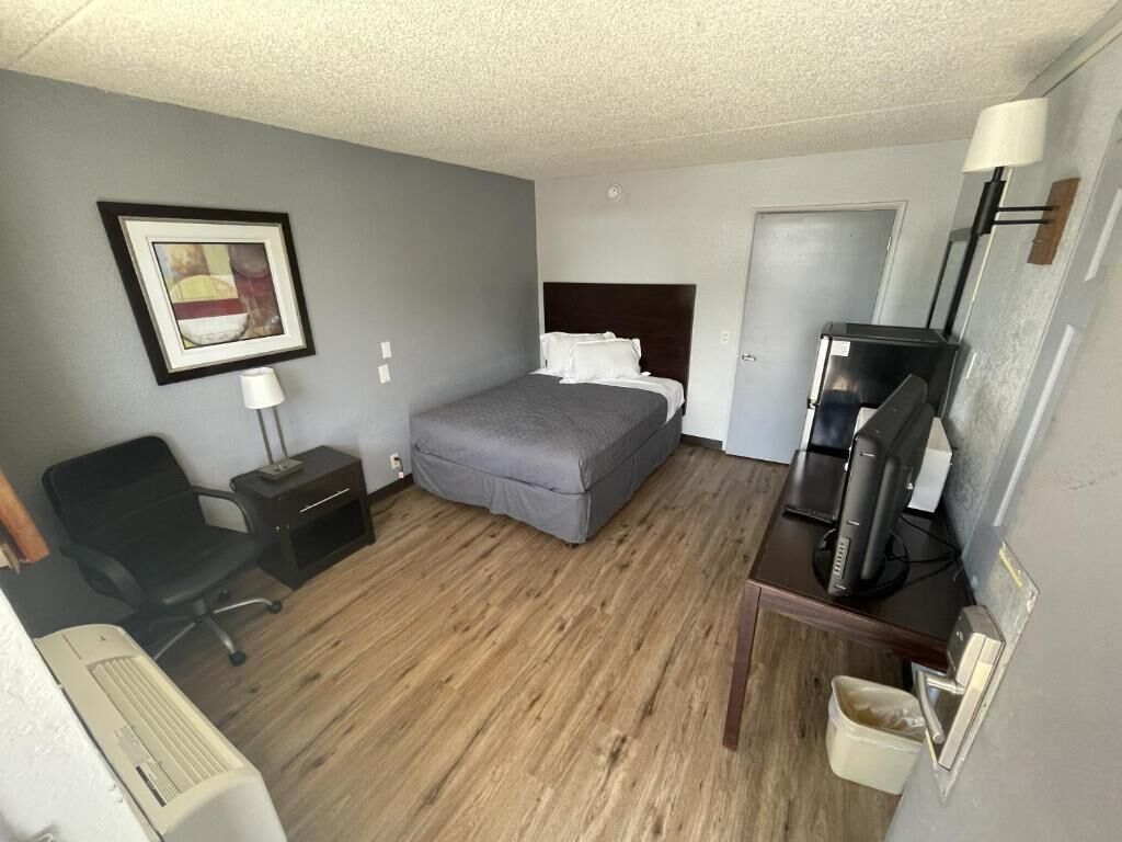A hotel room with a bed, a desk, a chair, a lamp, and a picture on the wall.