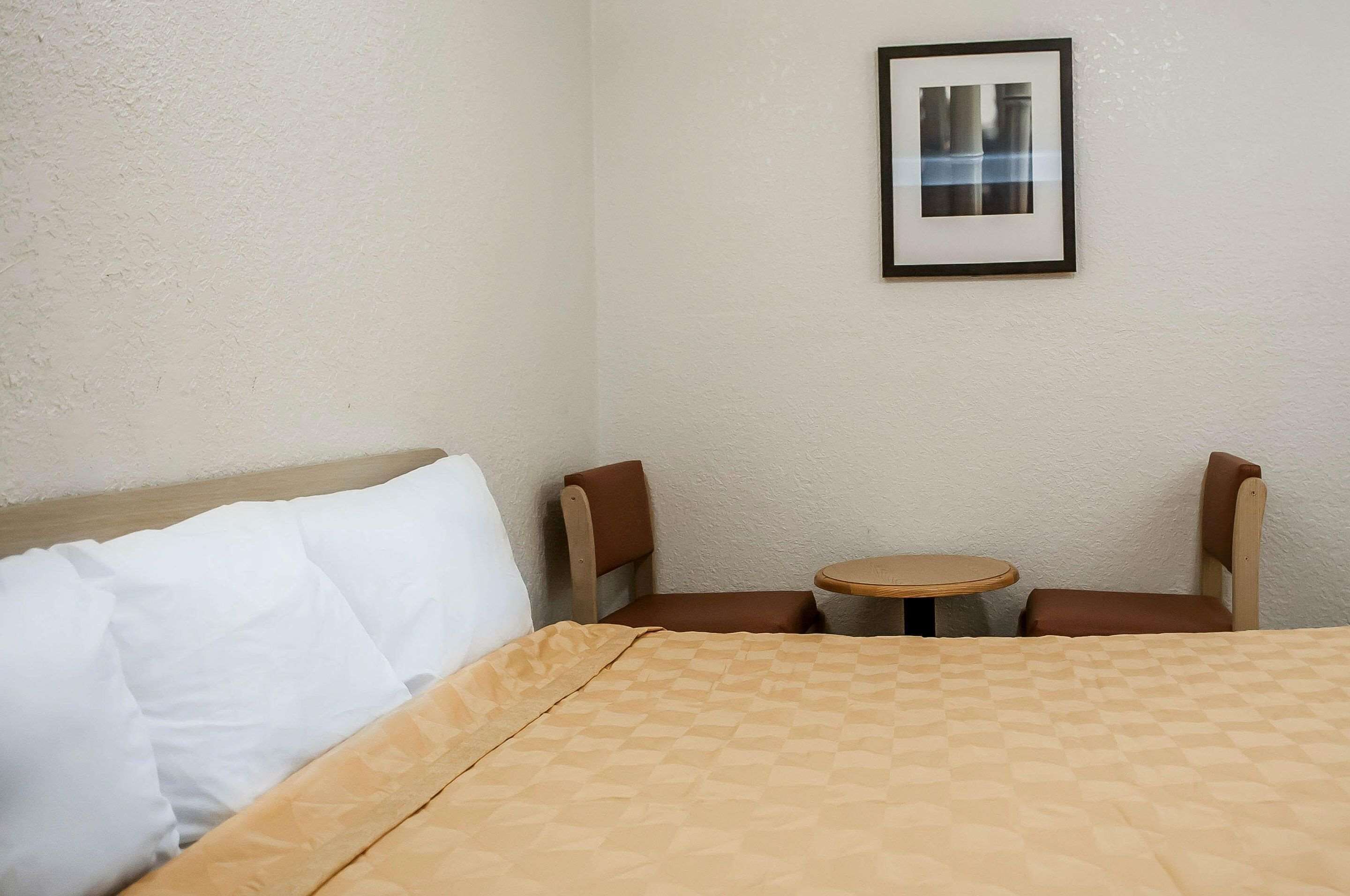 A hotel room with a bed, two chairs, a small round table, and a framed picture on the wall.