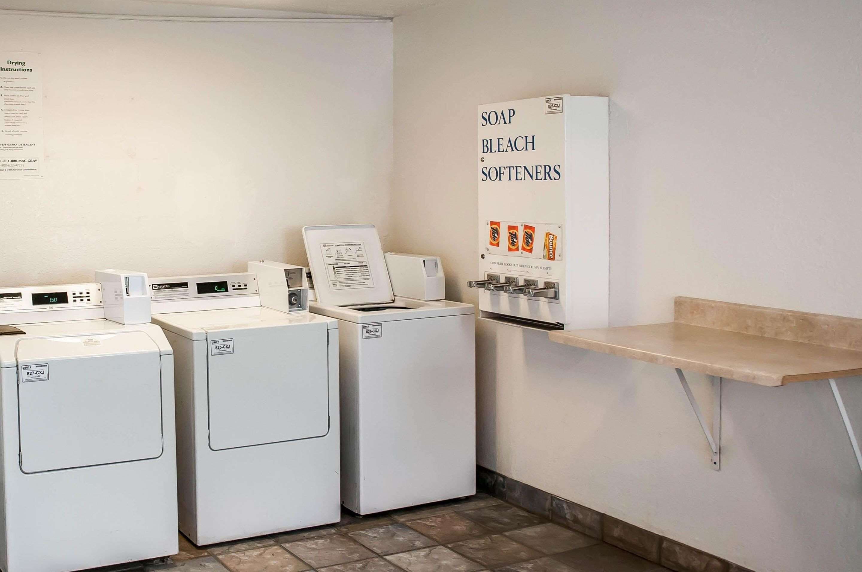 A laundry area with three washing machines, a drying rack, and a shelf with soap, bleach, and softeners.