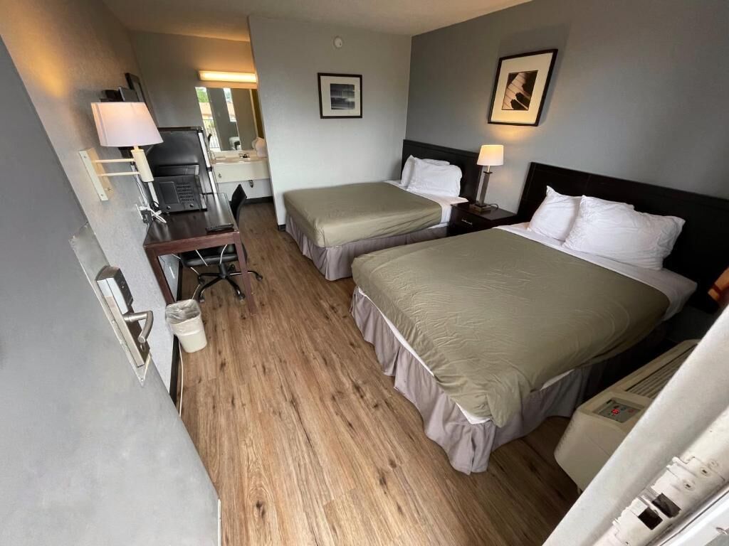 A hotel room with two single beds, a desk with a chair, a small table, and a mirror.