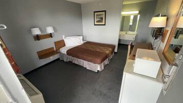 Et hotelværelse med seng, natborde, et spejl, et køleskab og et lille skrivebord.