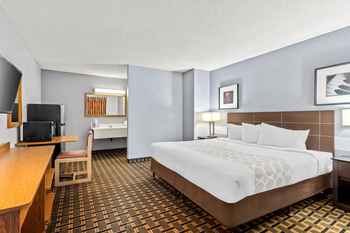 A hotel room with a bed, a desk, a chair, a television, a sink, and a mirror.