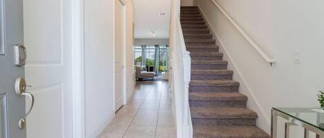 A hallway with a carpeted staircase, white walls, and a glass table on the right.