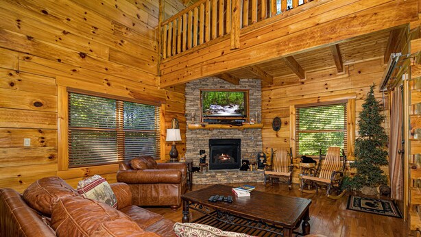 A log cabin interior with a stone fireplace, leather sofa, and wooden furniture. - Luxury cabin with private outdoor hot tub and access to resort pool (Sevierville)