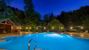 A swimming pool with a wooden deck, lounge chairs, and a covered area with umbrellas. - Luxury cabin with private outdoor hot tub and access to resort pool (Sevierville)