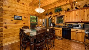 A wooden cabin interior with a dining table, chairs, kitchen appliances, and a ceiling light. - Luxury cabin with private outdoor hot tub and access to resort pool (Sevierville)