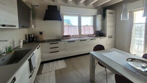 Une cuisine moderne avec des meubles blancs, une hotte noire et une fenêtre agrémentée de rideaux roses.